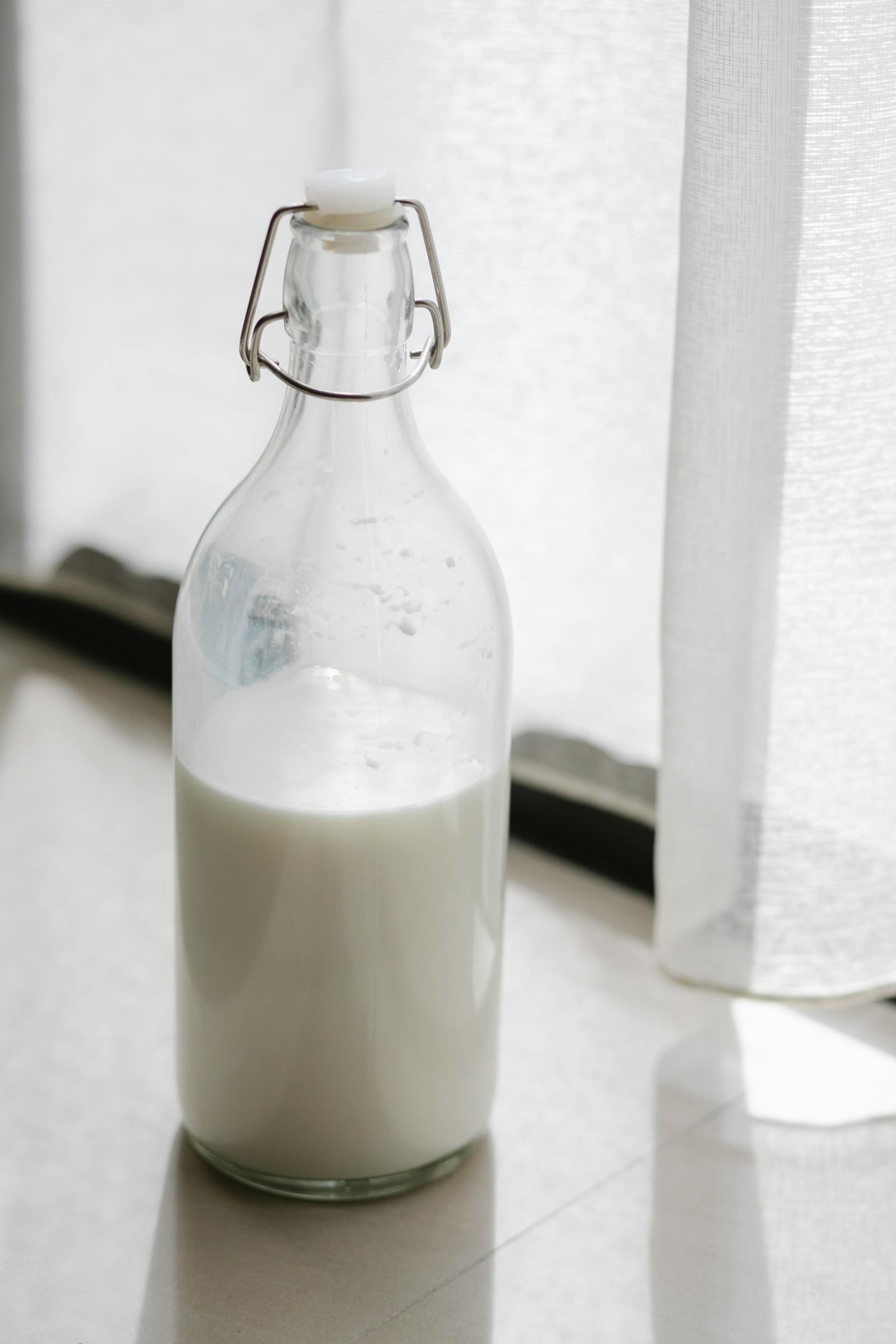 A NarvoMilk glass bottle catching warm morning light against the kitchen wall.